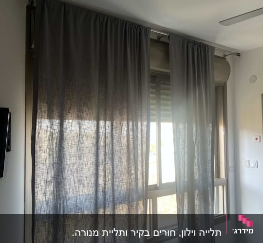 וילון אפור תלוי על מסילה מעל חלון